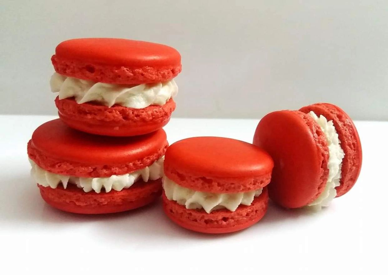 Four red macarons with white cream filling.