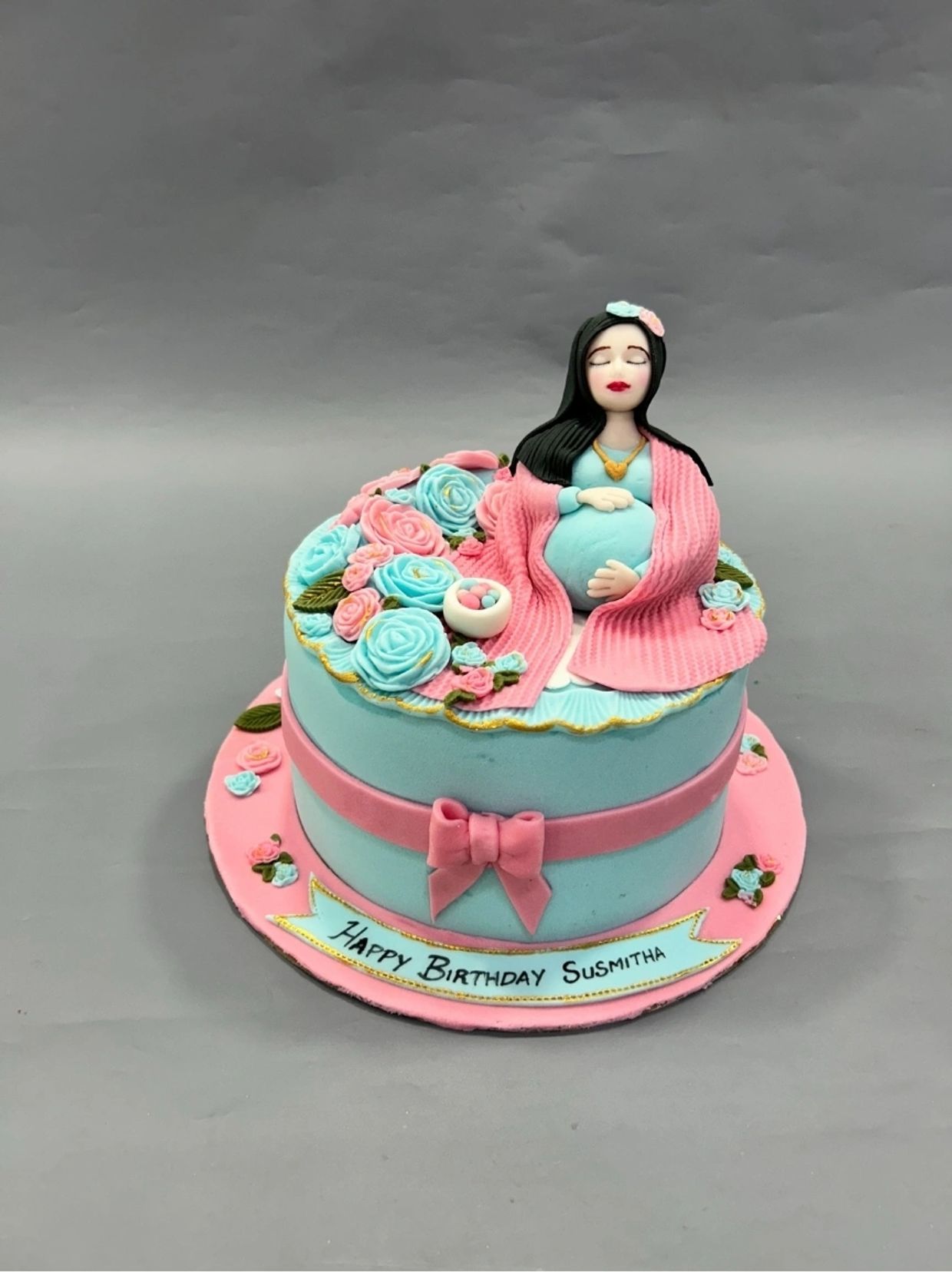 Pastel-colored birthday cake with a pregnant woman topper.