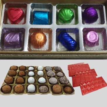 Box of assorted chocolates in colorful wrappers with unwrapped chocolates and red chocolate bars.