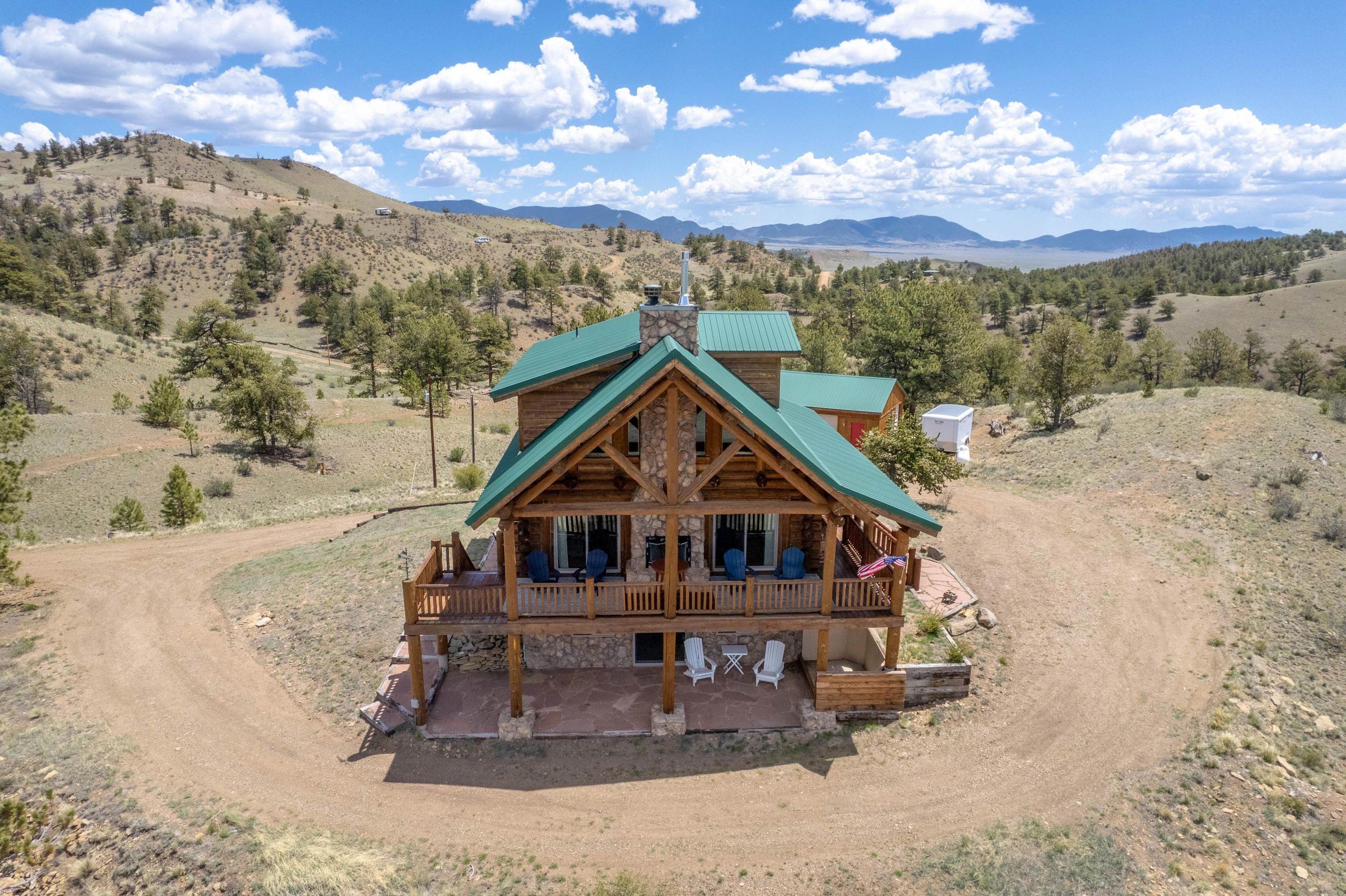 Log cabin with green roof surrounded by hills and trees under a partly cloudy sky.