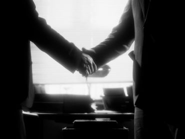 Two people shaking hands in a dark setting.