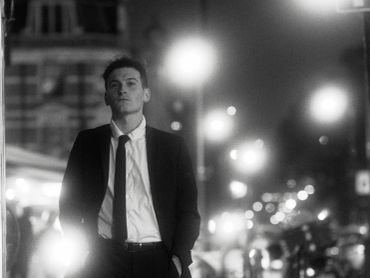 Man in a suit standing on a city street at night.