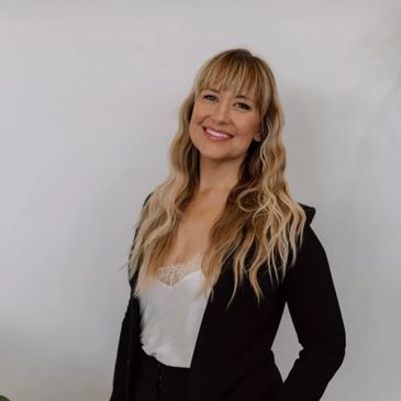 Smiling woman with long wavy hair wearing a black blazer and white top.