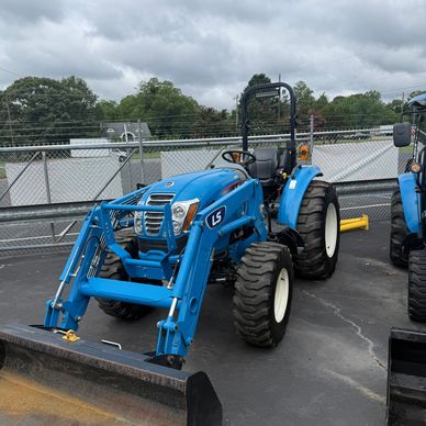 Blue tractor with front loader attachment in a parking lot.
