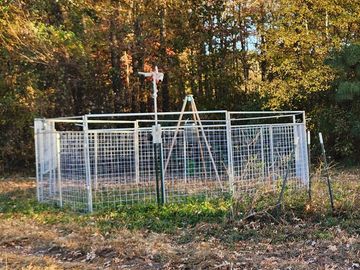 A fenced garden area with a weather vane in front of trees.