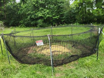 Net enclosure around a hole in a grassy field.