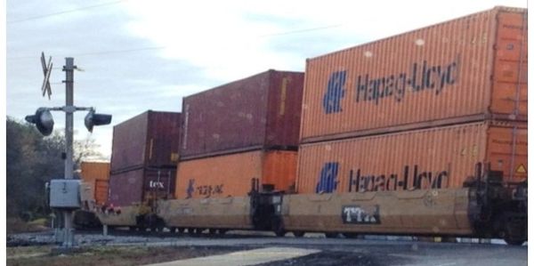 A freight train carrying stacked shipping containers crosses a road.