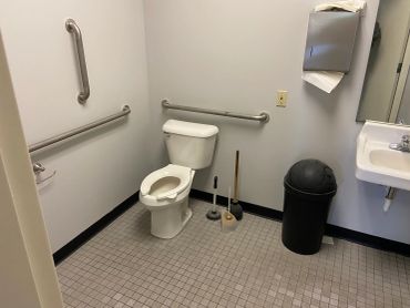 A clean, accessible public restroom with safety grab bars and cleaning tools.