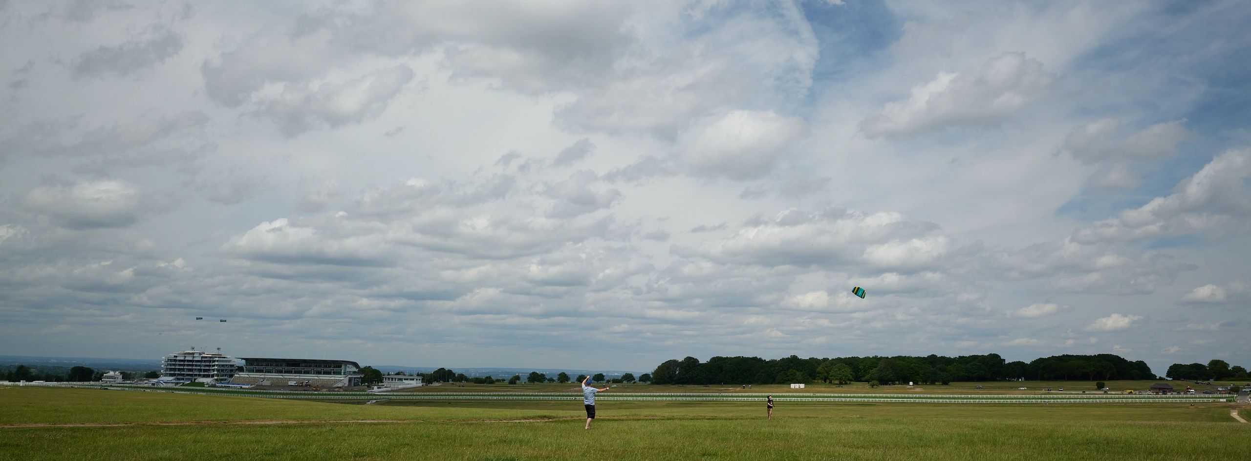 People flying a kite on a vast green field under a cloudy sky.
