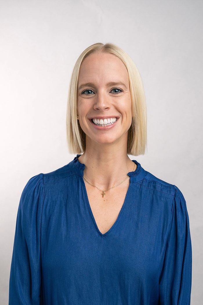 Smiling blonde woman wearing a blue blouse and a cross necklace.