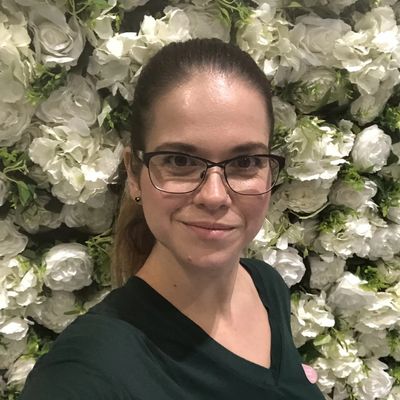 Lady wearing glasses standing in front of a white flower wall.