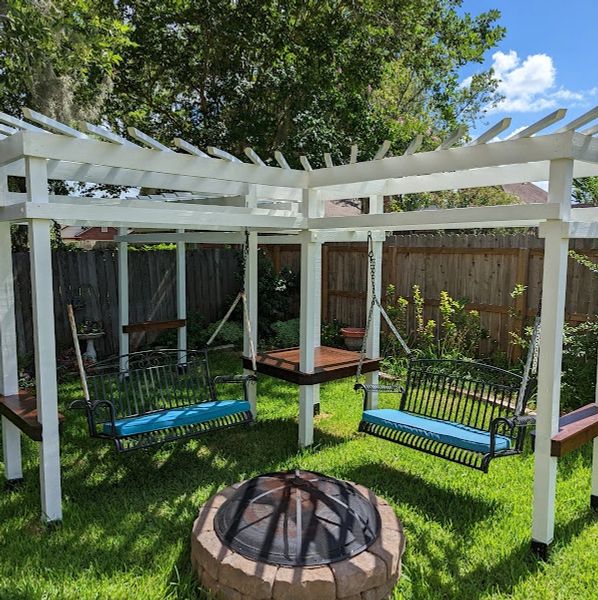 An image of two swings under a white pergola surrounding a round fire pit.