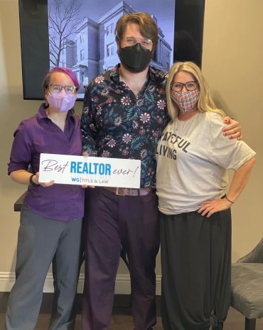 Three people wearing masks, one holding a "Best REALTOR ever!" sign.