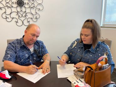 A man and woman signing documents at a table.