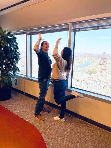 Two people high-fiving near a large window with city view.