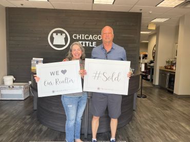 Happy clients hold signs celebrating their realtor and home sale at Chicago Title office.