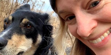 Smiling woman taking a close selfie with a black and tan dog outdoors.