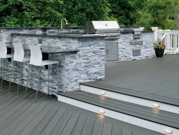 Outdoor stone bar with white stools and deck lighting.