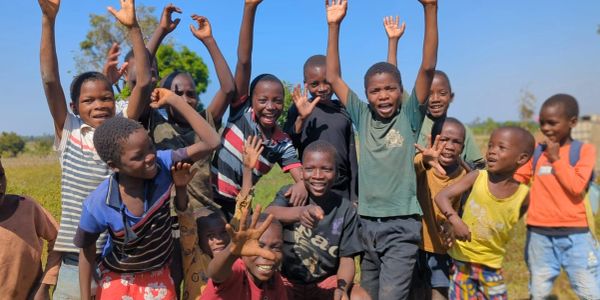 Group of happy children raising hands outdoors.