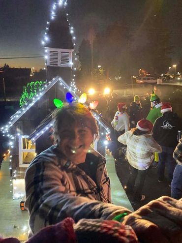 Person wearing colorful Christmas lights on head at a festive nighttime event.