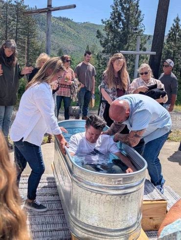 Person being baptized outdoors in a metal tub with group support.