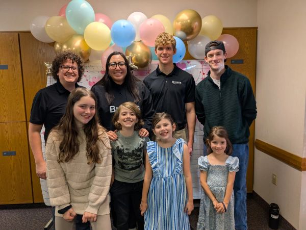 A group of smiling people posing indoors with colorful balloons behind them.