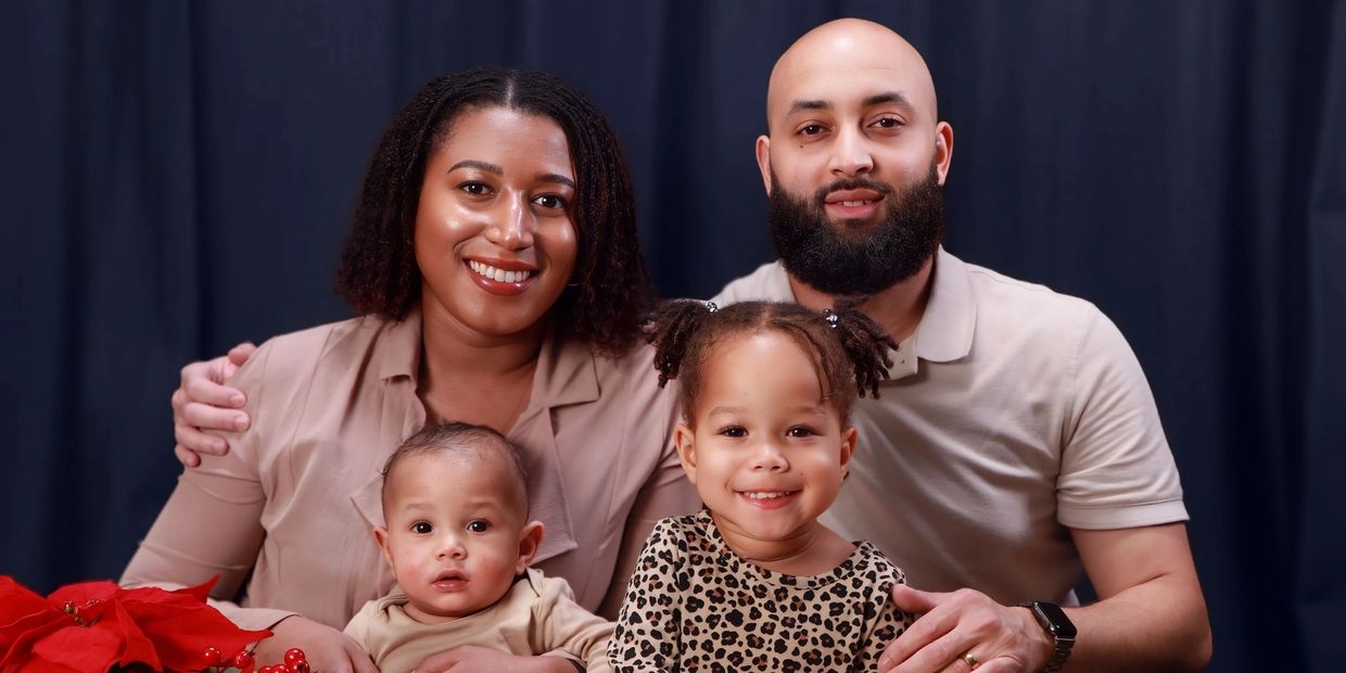 Smiling family portrait with two kids and parents against a dark backdrop.