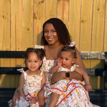 Mother with two children in matching floral dresses sitting outdoors.