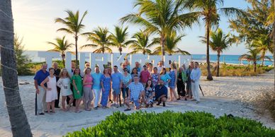 Group photo of people at a beach with palm trees and a welcome sign.