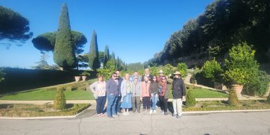 Group of people posing outdoors in a sunny garden with manicured trees.