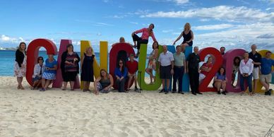 Group of people posing on a sandy beach by large colorful Cancun 2023 letters.