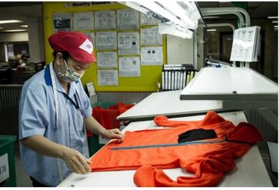Worker inspects an orange garment on a quality control table.