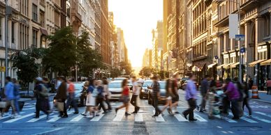Busy city street with people crossing at sunset.