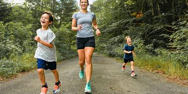 A woman and two children joyfully running on a forest trail.