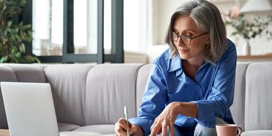 Older woman working on a laptop and taking notes at home.