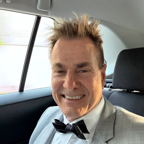 Smiling man in a gray suit and black bow tie inside a car.