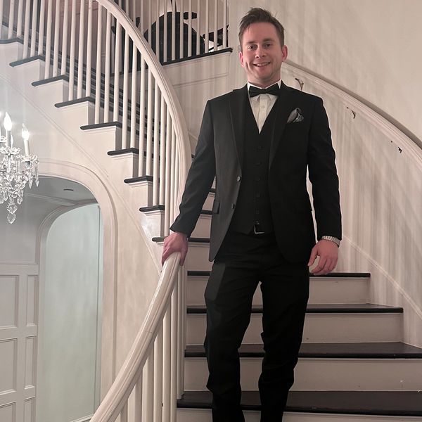 Man in black tuxedo standing on a staircase.