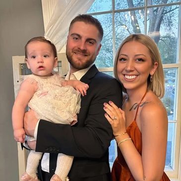 A happy couple with their baby, smiling indoors near a window.