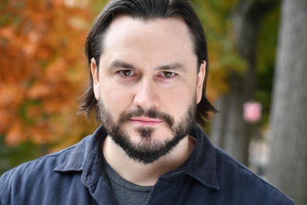 Man with a beard and intense gaze outdoors.