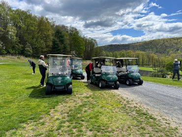 Golfers preparing near golf carts on a green course under a cloudy sky.