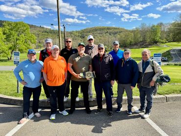 Group of men posing outdoors on a sunny day, one holding a trophy.