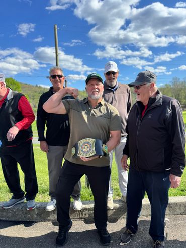 Group of men outdoors, one flexing muscles and holding a championship belt.
