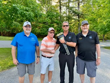 Four men standing outdoors, one holding a championship belt.