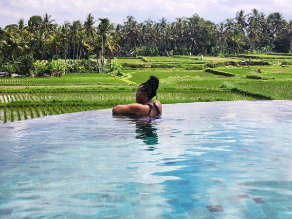 A woman relaxing in an infinity pool overlooking lush green rice fields.