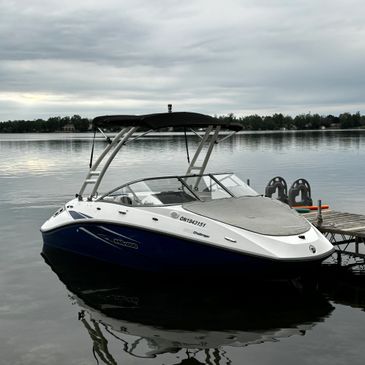 A sleek white and blue motorboat docked on a calm lake under a cloudy sky.