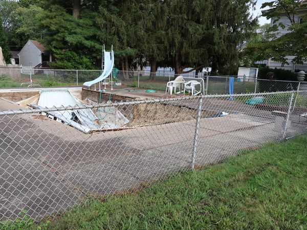 An empty, deteriorating swimming pool surrounded by a chain-link fence.