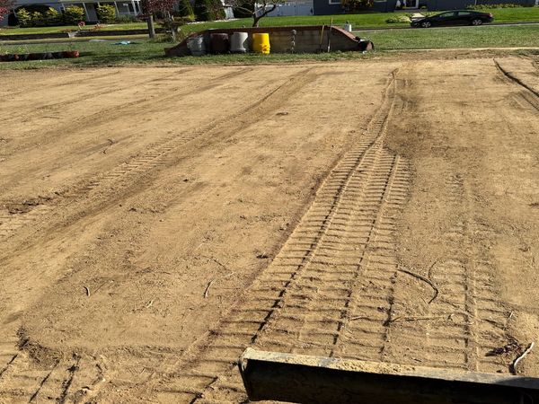 Freshly leveled dirt with tractor tire tracks and a few trash bins in the background.