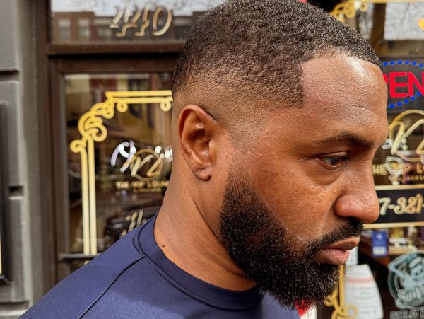 Close-up of a man with a fresh haircut and beard outside a barbershop.