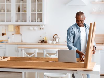 Man assembling furniture while watching instructions on a laptop.