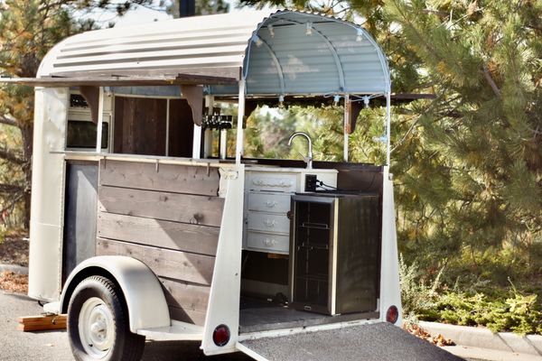 Cream colored horse trailer converted to mobile bar equipped with four keg taps